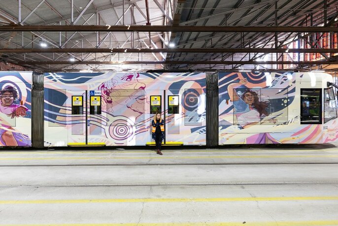 A tram painted with artworks, parked in an undercover tram terminus.