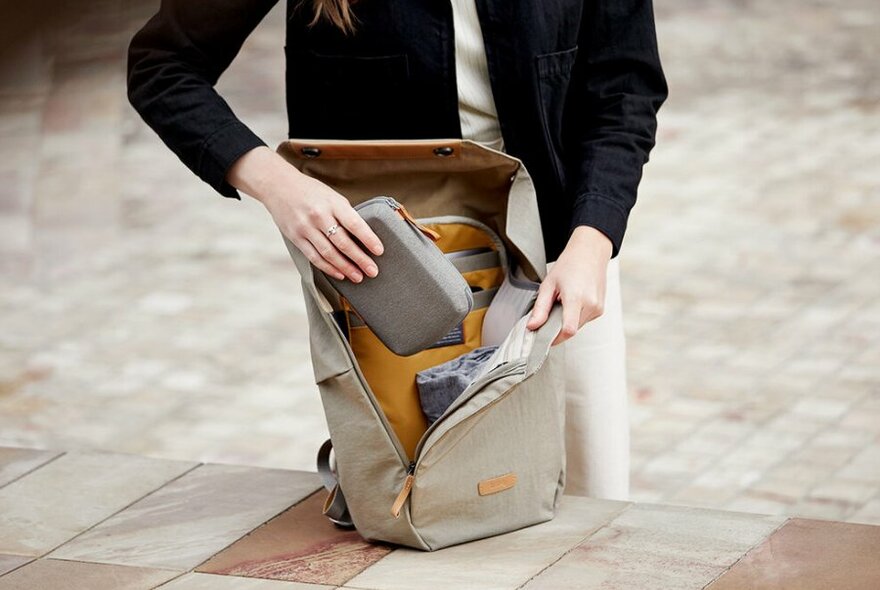 A woman wearing all black packing small items into her grey backpack