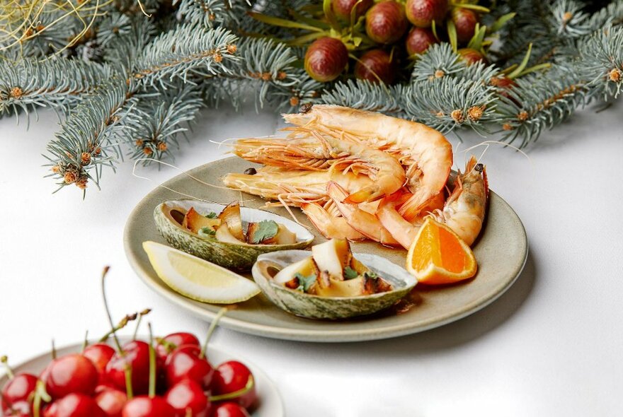 A Christmas-themed table setting with a plate of prawns and a bowl of cherries. 