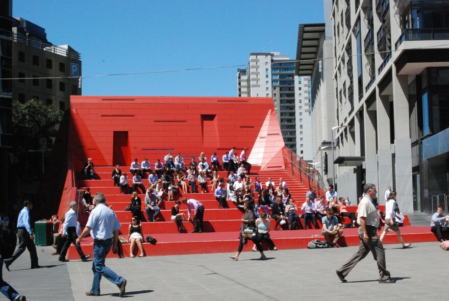 People sitting on futuristic red stair amphitheatre at Queensbridge Square.
