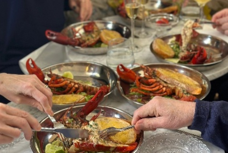 Silver bowls of seafood with people using cutlery to serve.