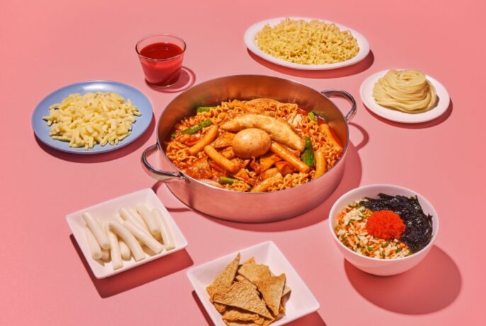 A large copper pan filled with noodles and chicken, with smaller plates of food and condiments arranged around it.