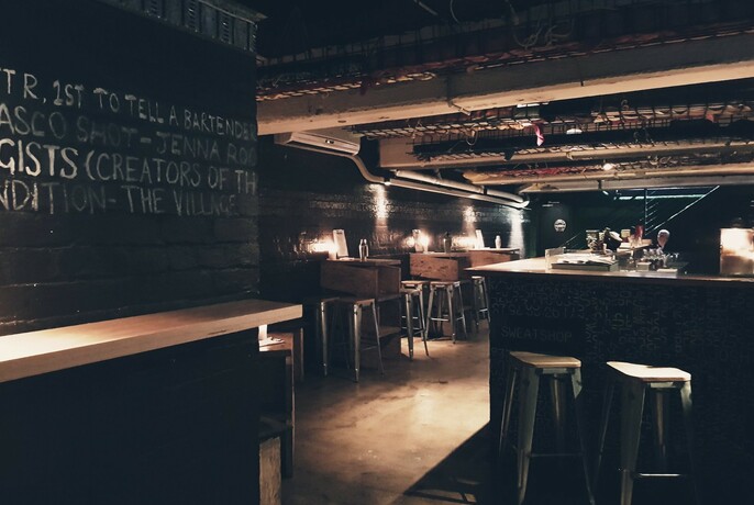 Empty interior of Sweatshop Bar with bar stools and low lighting.