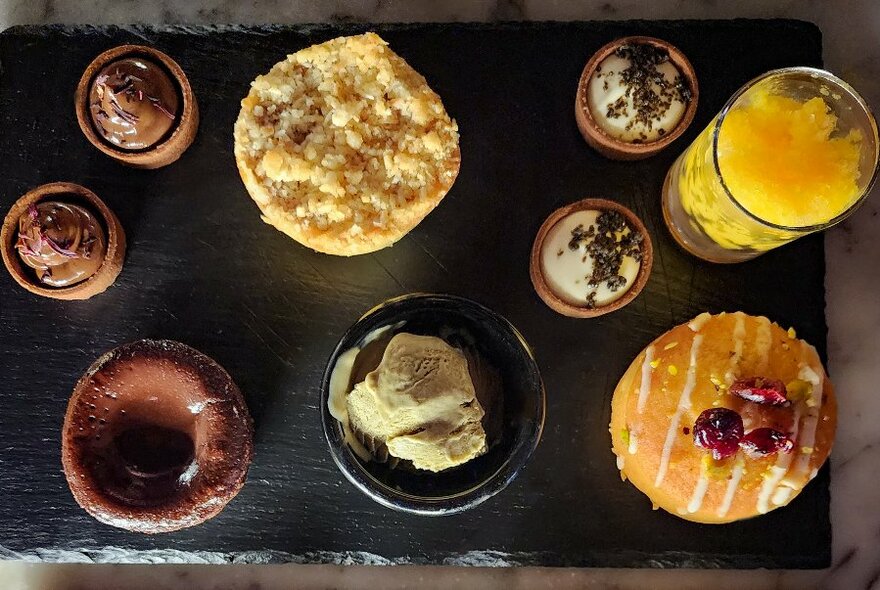 A black platter with round dishes and treats.