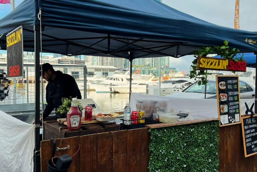 A market food stall with a blue canopy and person cooking. 