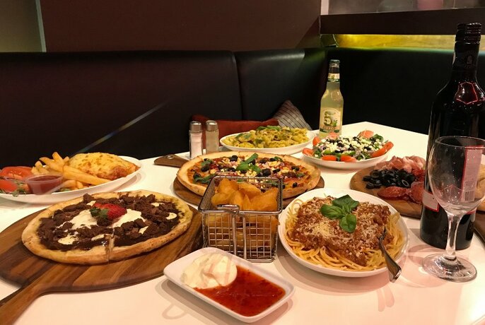 Table of food that includes a plate of spaghetti with meat sauce, three pizzas, chips and an antipasto selection on a board.