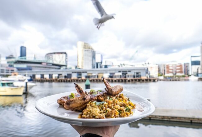 A plate of chicken and rice held out over water views at a restaurant.