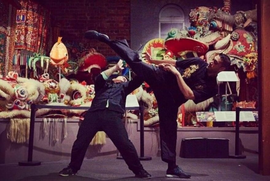 Two kung fu martial artists in performance mode in front of a museum exhibition display.