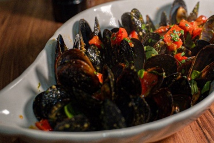 A bowl of mussels with tomatoes.