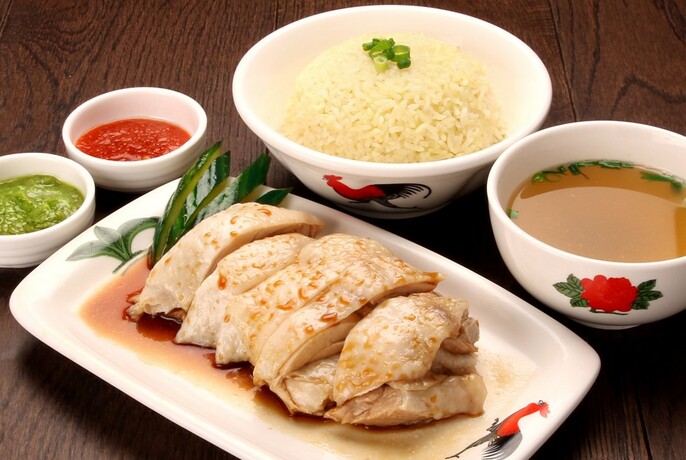 Sliced chicken on a white plate surrounded by white bowls of rice and condiments.