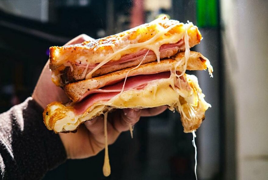 Hand holding a croque monsieur toasted sandwich containing melted cheese and ham.