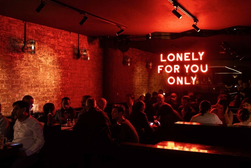 People in a basement bar lit by a red neon sign. 