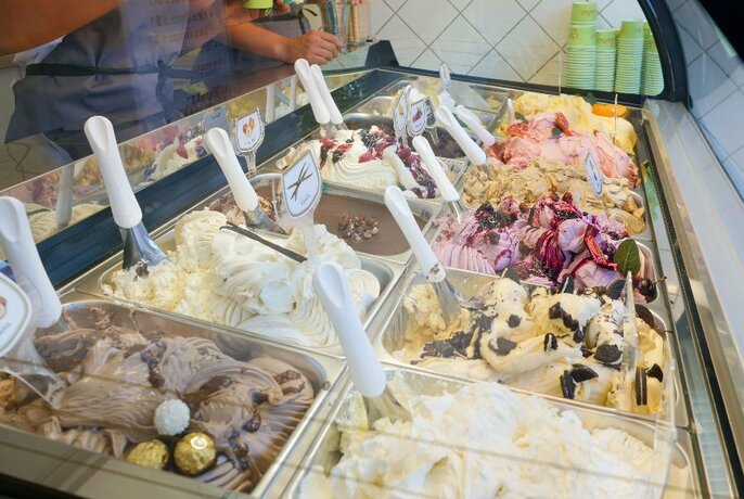 Tubs of different gelato in a refrigerated glass display cabinet.