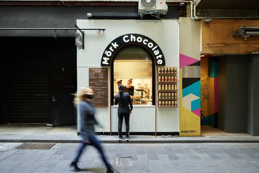 External of Mork Chocolate window, with customer and server at window, and blurred pedestrian walking past.
