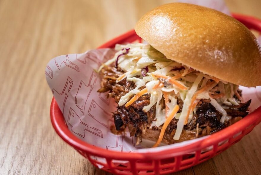 A burger with slaw in a red basket. 