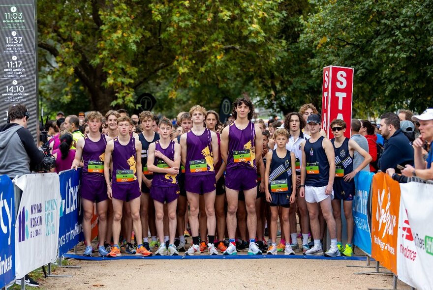 A team of runners wearing matching purple athletic shorts and tops, lined up in a row at the start of a run.