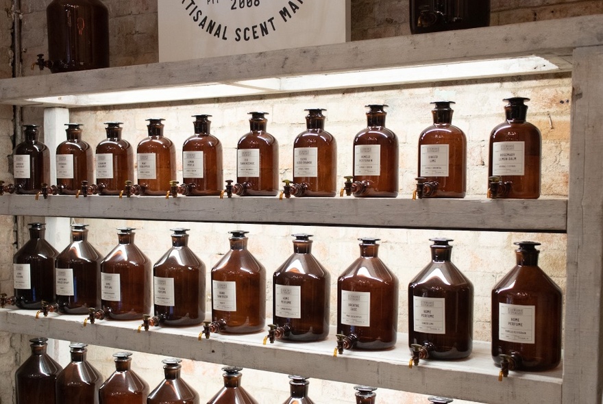 A wall lined with three shelves of large amber bottles with taps.