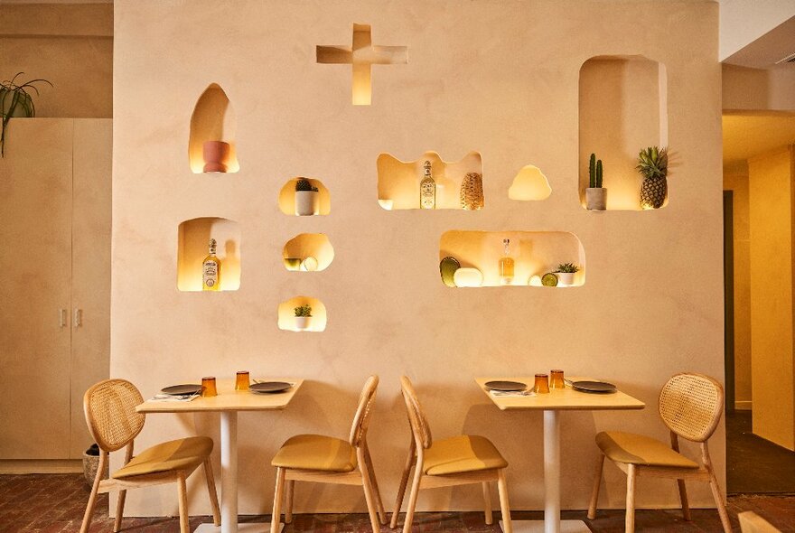 Restaurant interior with tables and chairs in front of a pale pink wall with backlit display insets.