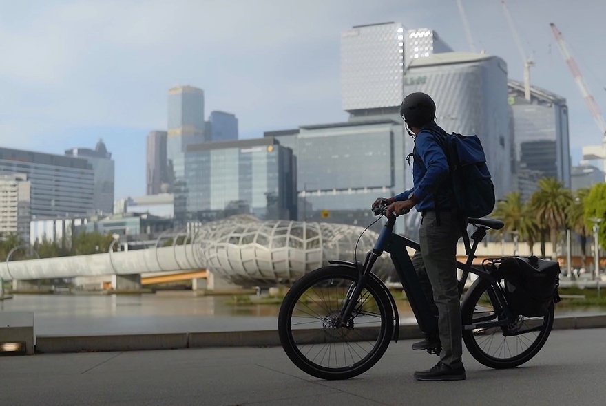 Man standing and straddling an e-bike and looking over his shoulder at the city view behind him.
