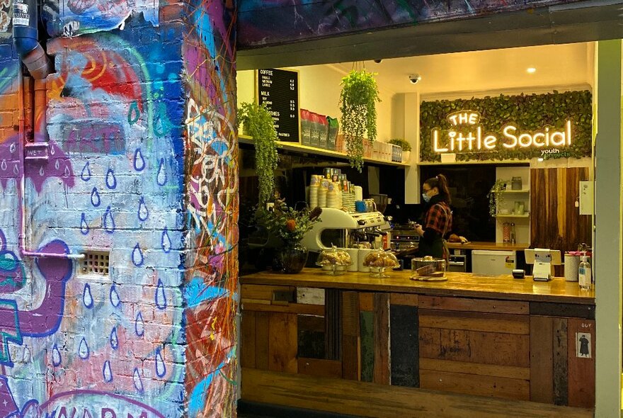 Looking into the interior of a small cafe kiosk in Hosier Lane from the street, with street art on the brick wall to the left of the image.