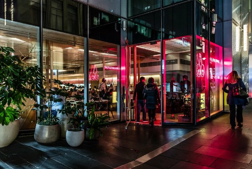 Couple walking into a city restaurant with potted plants lining the facade.