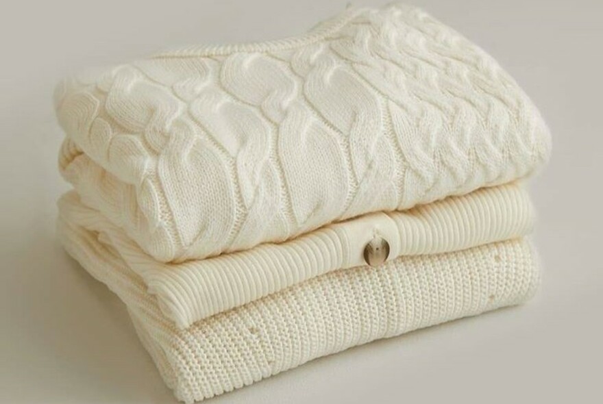 Three cream knitted sweaters folded on a white background.