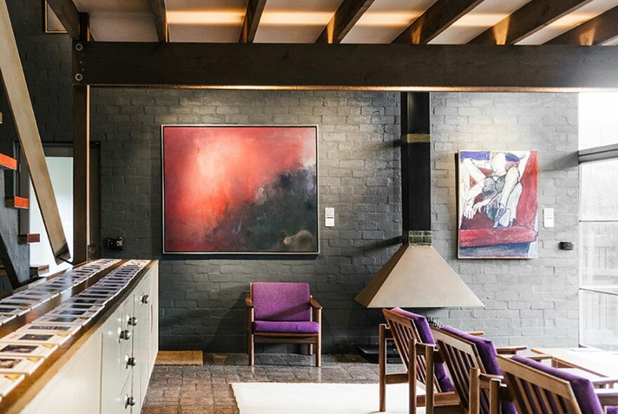 The interior of a house with beams on the ceiling, artwork on the walls and a purple chair. 