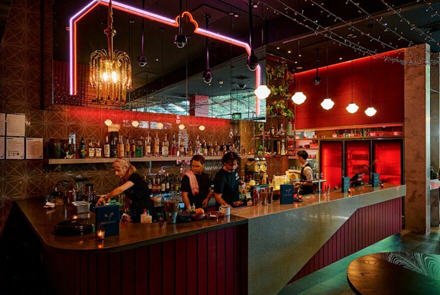 A red-lit bar with four bartenders in a large space.