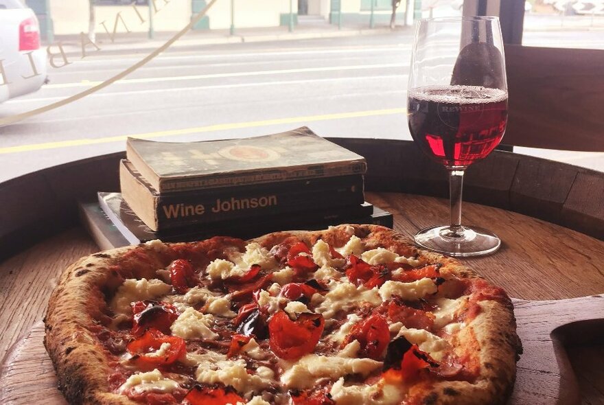 Plate of pizza and a glass of wine on a window table with view onto street.