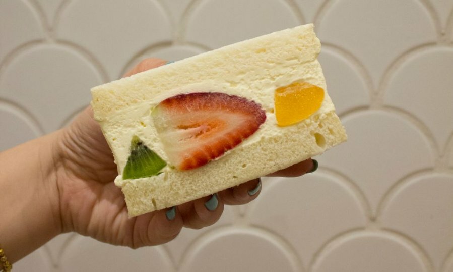 Hand holding fruity cream sando on it's side, showing inside filled with cream and fruit