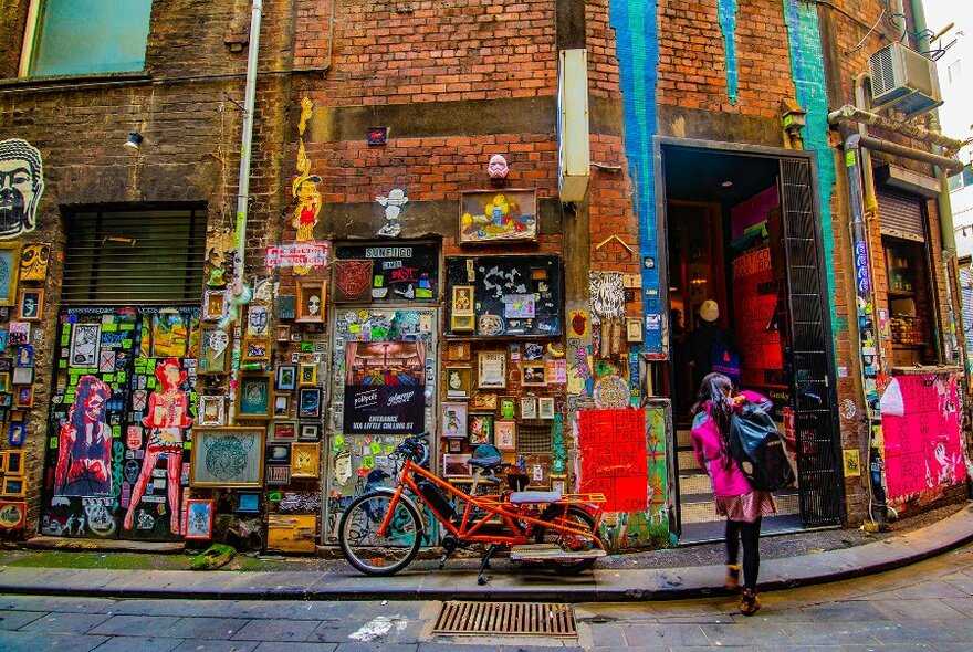 A woman walking into a shop in a street art covered laneway, with tiny picture frames covering the walls.