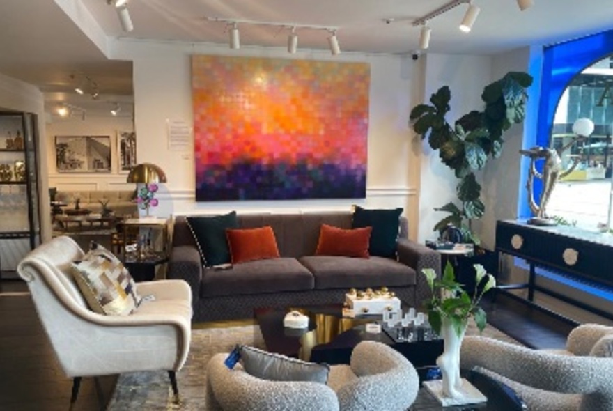 Interior of a store with couches, armchairs, lamps and paintings on display and for sale.