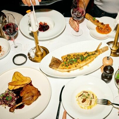 An array of opulent Parisian dishes presented on white plates, on a white table with gold candlesticks, white candles and wine glasses.