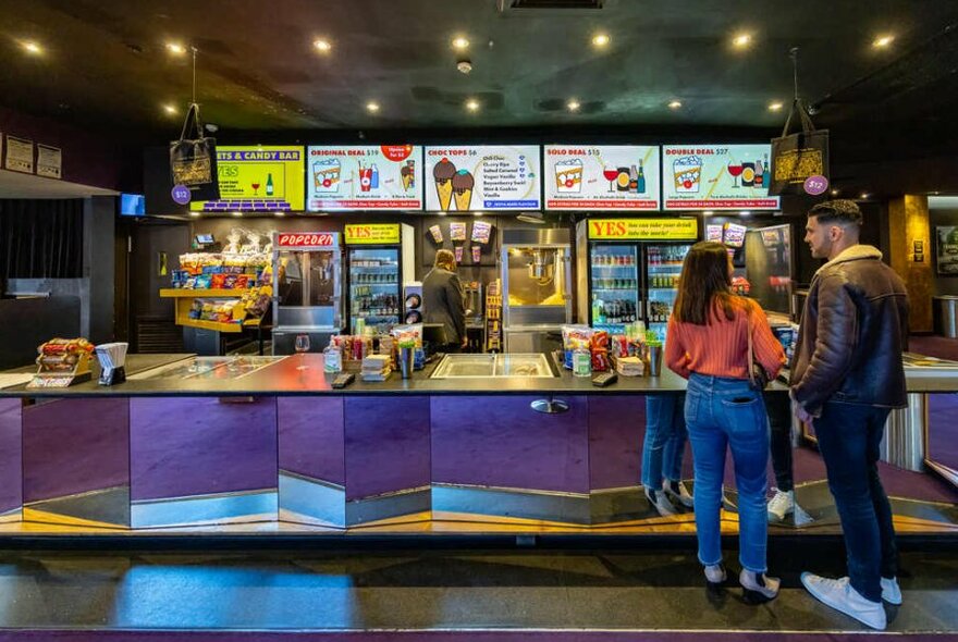 A couple ordering from a candy bar at a movie theatre.