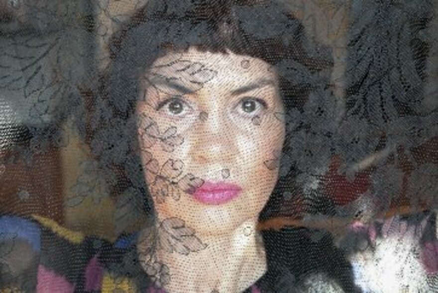 Singer Jackie Bornstein with short bobbed hair and pink lipstick, viewed behind a sheer lace screen.