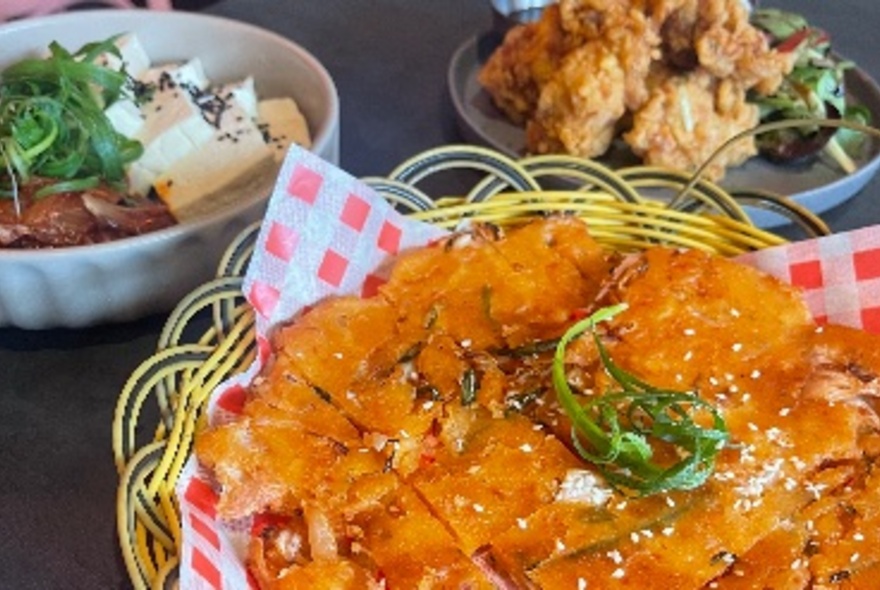 A basket of Korean food next to dishes of tofu and fried chicken.