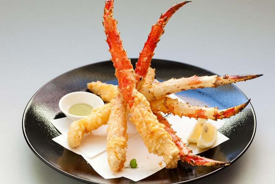 Black dish with battered crab legs and condiments.