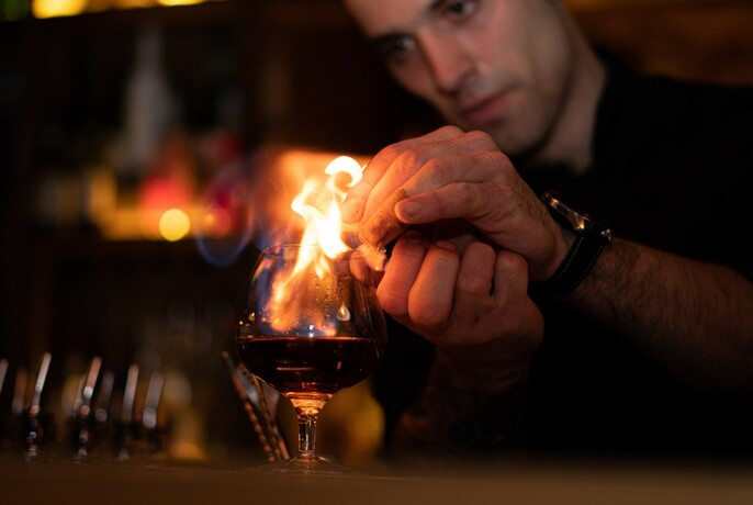 Close up shot of a bartender setting a cocktail alight. 