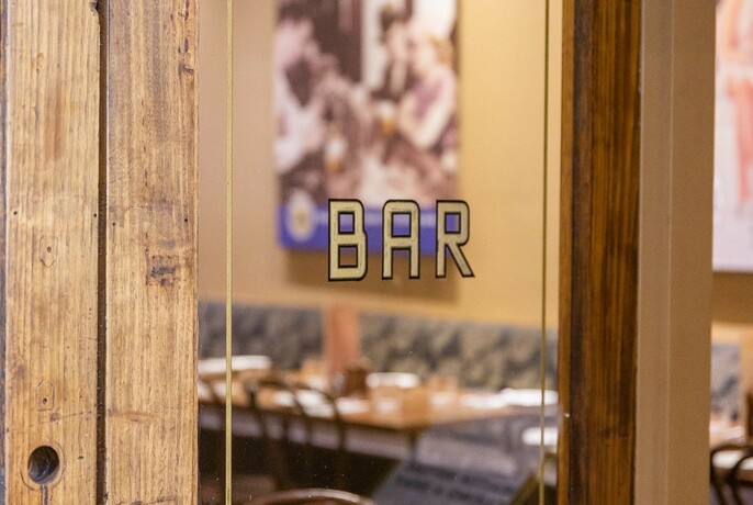 Closeup of a glass door with the word bar written on it in gold lettering.