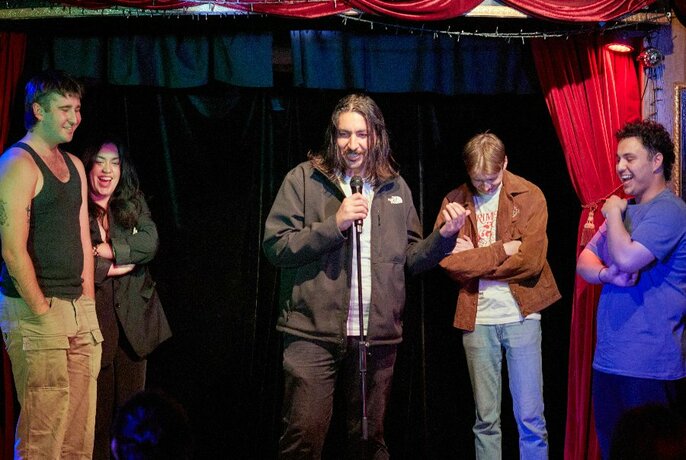 A group of comedians surrounding a man holding a microphone onstage.