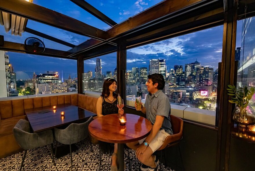A couple drinking on a rooftop bar at sunset.