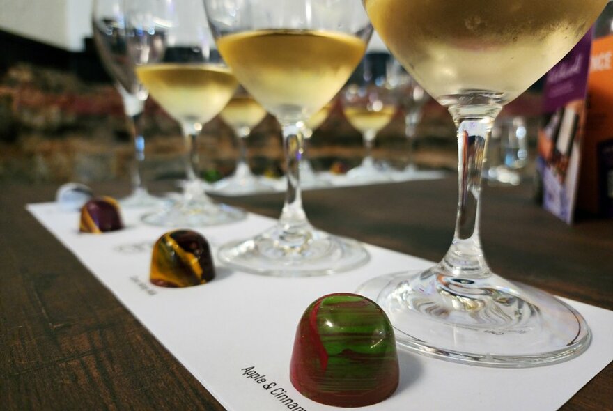 Four small pours of wine in glasses on a counter with a small chocolate in front of each one.