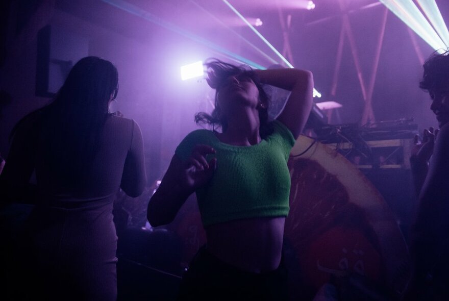 People dancing in a dark nightclub with purple lights.