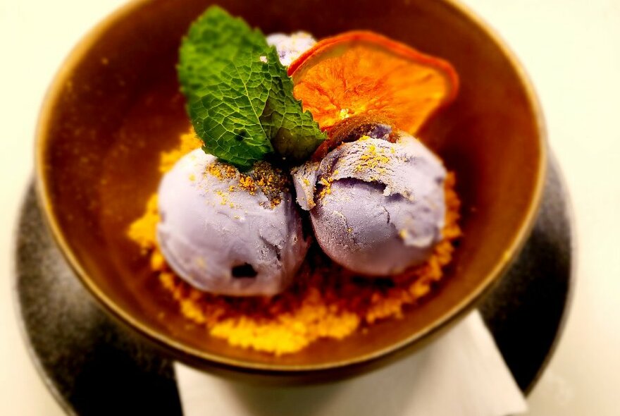 A bowl of purple ice cream with a slice or orange and mint leaf.