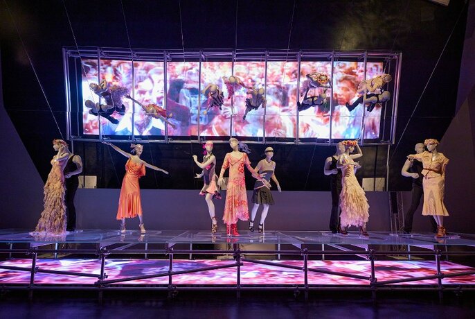 A gallery display of fashion on dancing mannequins with a digital art backdrop.
