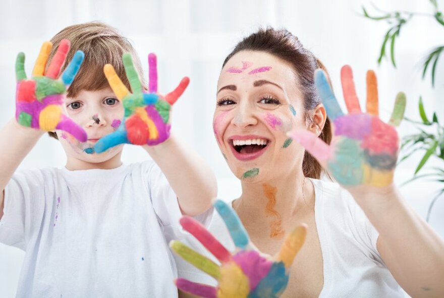 A young child and a woman holding up their hands which are covered in rainbow colours. 