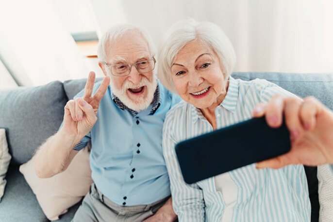Older couple seated on a couch taking a selfie with a smartphone.