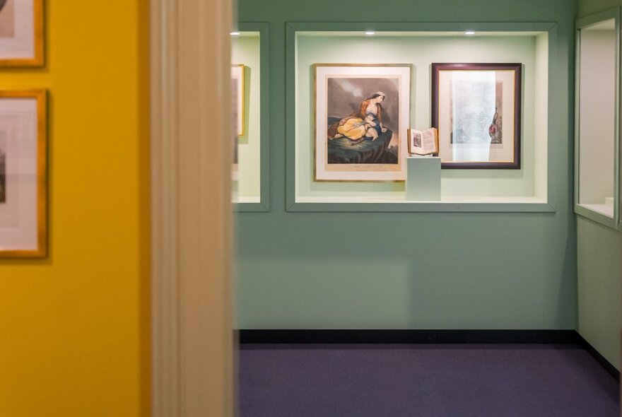 A green exhibition room viewed through the doorway of a yellow room, with display cases of artworks and artefacts.