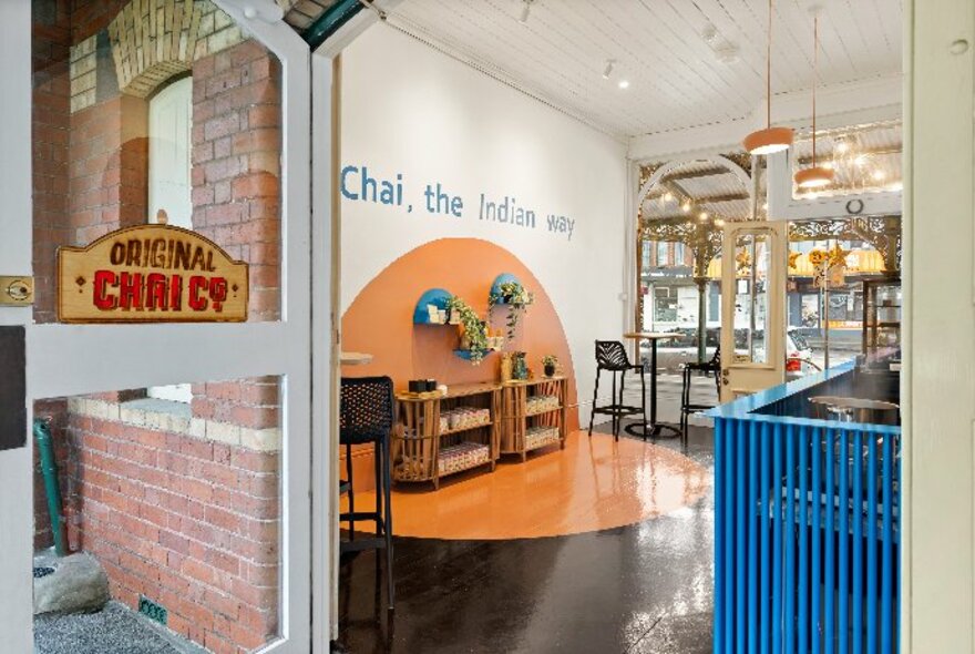 Looking through the entrance into the Original Chai Co cafe and shop, with a view of the service counter, tables and chairs.