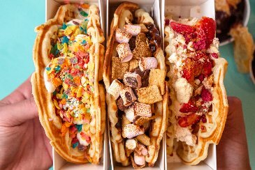 Three waffles, seen from above, lined up with a variety of sweet and savoury toppings.